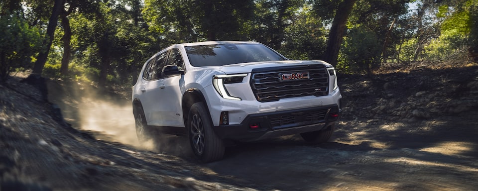 2024 GMC Acadia AT4 traversing through rough terrain in the forest.