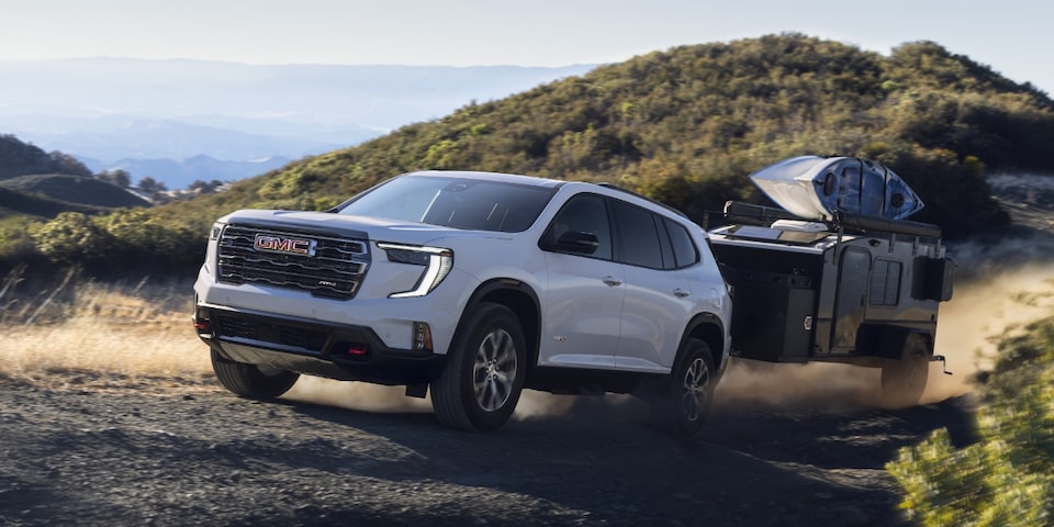  2024 GMC Acadia AT4 towing a trailer through rough terrain.