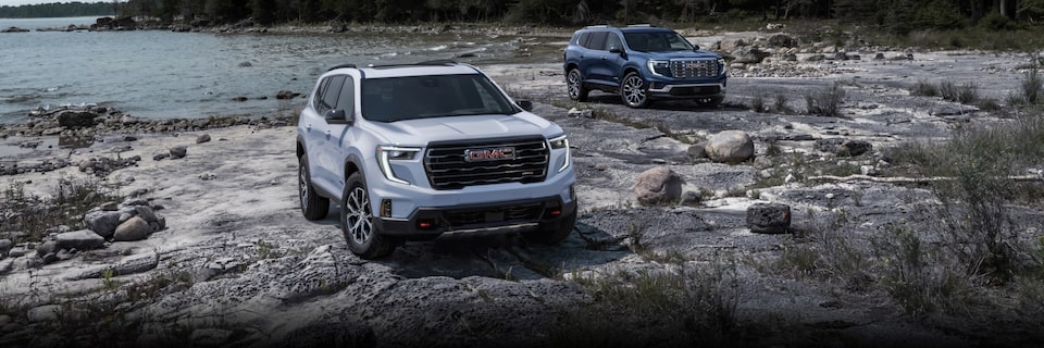 Two models of the 2024 GMC Acadia parked by the lakeside.