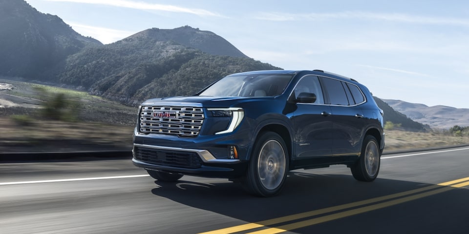 Side view of the 2024 GMC Acadia Denali driving alone on a hillside road.