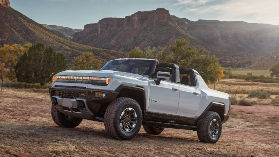 Front three-quarters view of a 2025 GMC Hummer EV Pickup Truck parked uphill overlooking mountains.