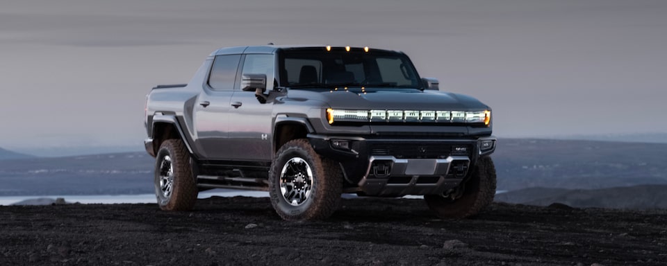 Wide front three-quarters view of the 2025 GMC Hummer EV Pickup Truck parked alone during dusk.