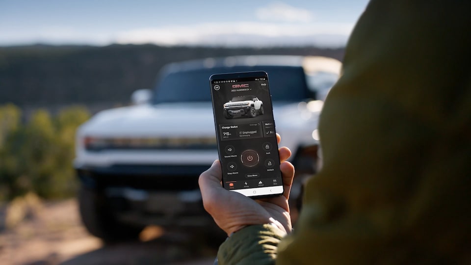 Close-up view of a person utilizing the myGMC Mobile App with the 2025 GMC Hummer EV parked in the background.