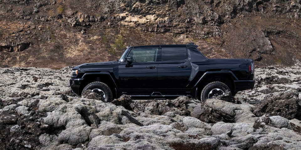 Side view of a black 2025 GMC Hummer EV Pickup Truck parked in the rocky mountains.