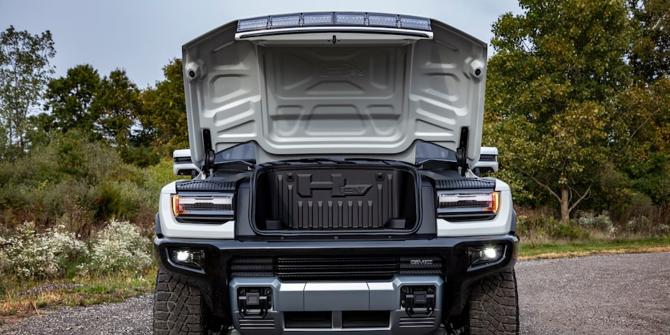 Front view of a GMC Hummer EV SUV with its front hood open on a road.