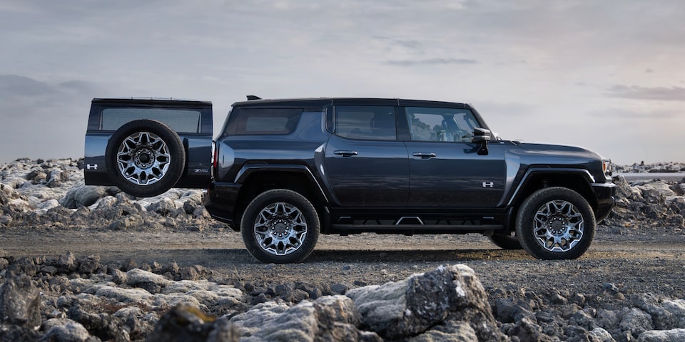 Side view of a black GMC Hummer EV SUV  on a rocky plain with the trunk door opened.