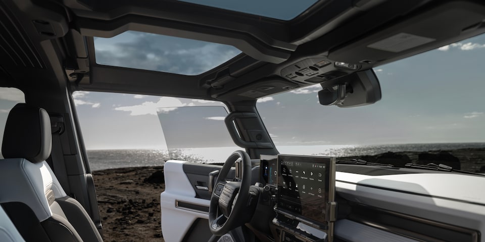 Side interior front view of a 2025 GMC Hummer EV SUV with the front door opened on the beach.