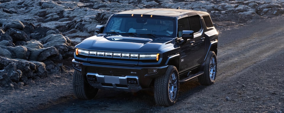 Three-quarters view of a 2025 GMC Hummer EV SUV going down the road surrounded by rocks.