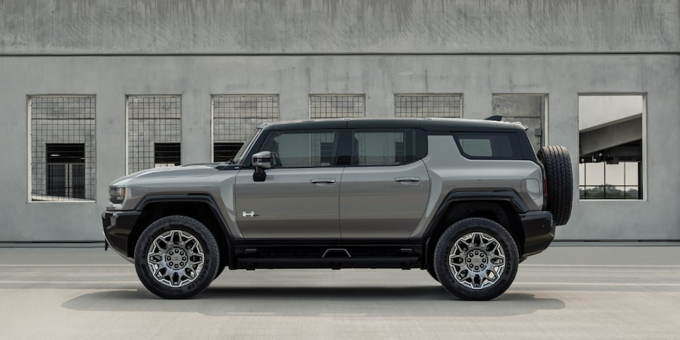 Side view of a gray 2025 GMC Hummer EV SUV parked next to a building.