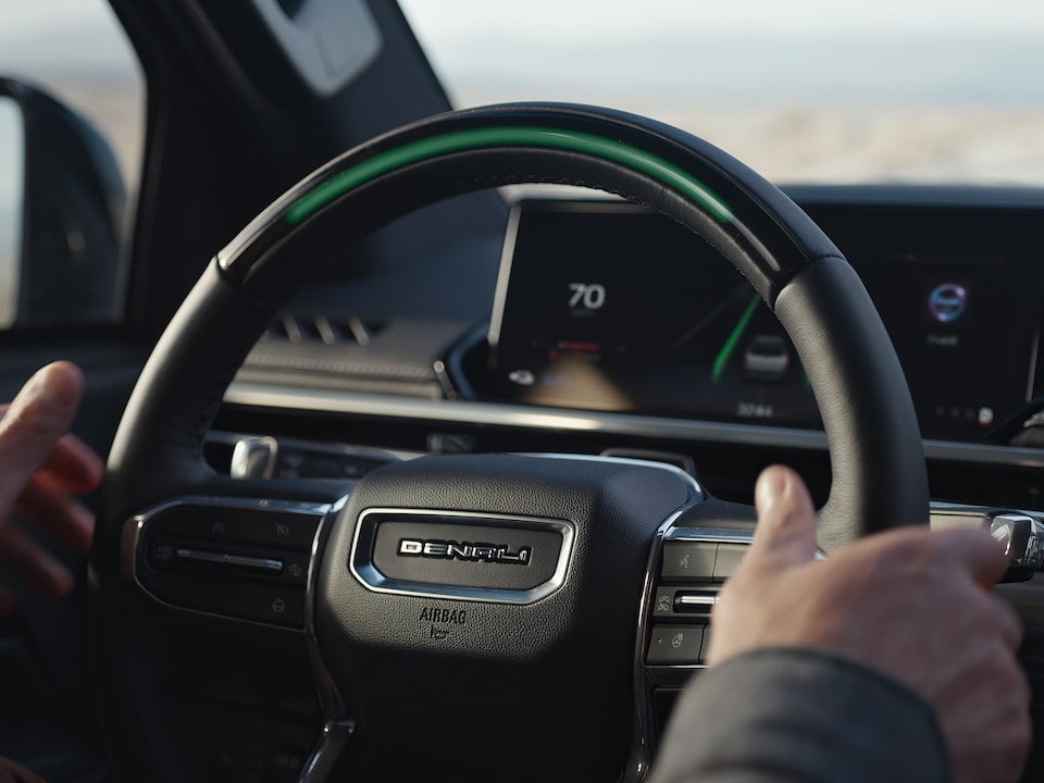 Close up view of a person's hand on the steering wheel of the 2025 GMC Sierra EV Denali.