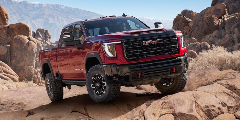 Front-side view of a 2025 GMC Sierra HD AT4X AEV truck parked on a rocky terrain.