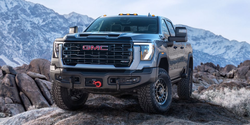 Front-side view of a 2025 GMC Sierra HD AT4 truck parked in front of snow-covered cliffs.