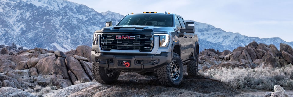 Front-side view of a 2025 GMC Sierra HD AT4 truck parked in front of snow-covered mountains.