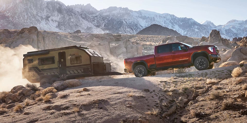 Side view of a 2025 GMC Sierra HD AT4 truck hauling a small trailer through a rocky terrain.