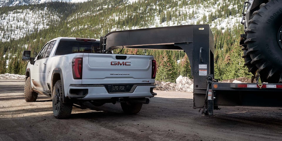 Back-side view of a 2025 GMC Sierra HD AT4 hauling a large trailer on the road.