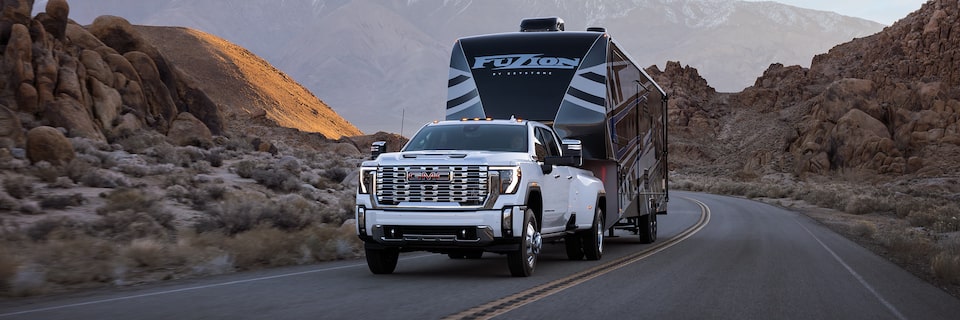 Wide Front Three-Quarters View of a 2025 GMC Sierra HD Denali Hauling a Trailer Through the Mountains at Dusk