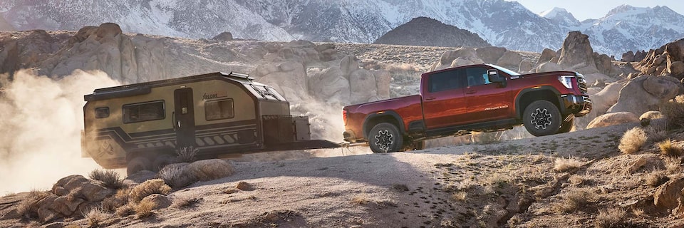 A 2025 GMC Sierra HD truck towing a trailer thorugh a rocky terrain.