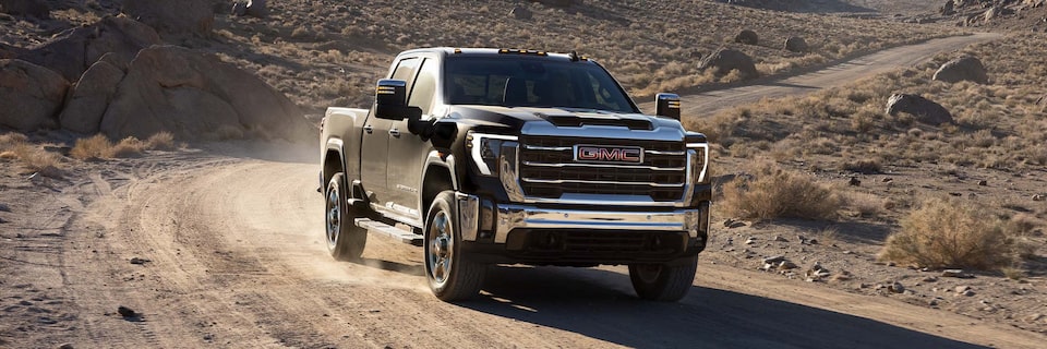 Vue latérale avant élargie du camion GMC Sierra HD Pro/SLE/SLT 2025 en mouvement sur une route dans un désert.