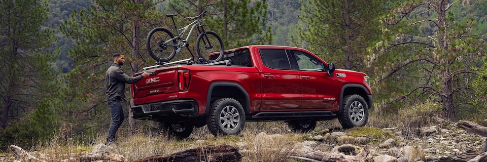 GMC Sierra AT4 Parked Off-Road as a Man Unloads his Bike From the Truck Bed