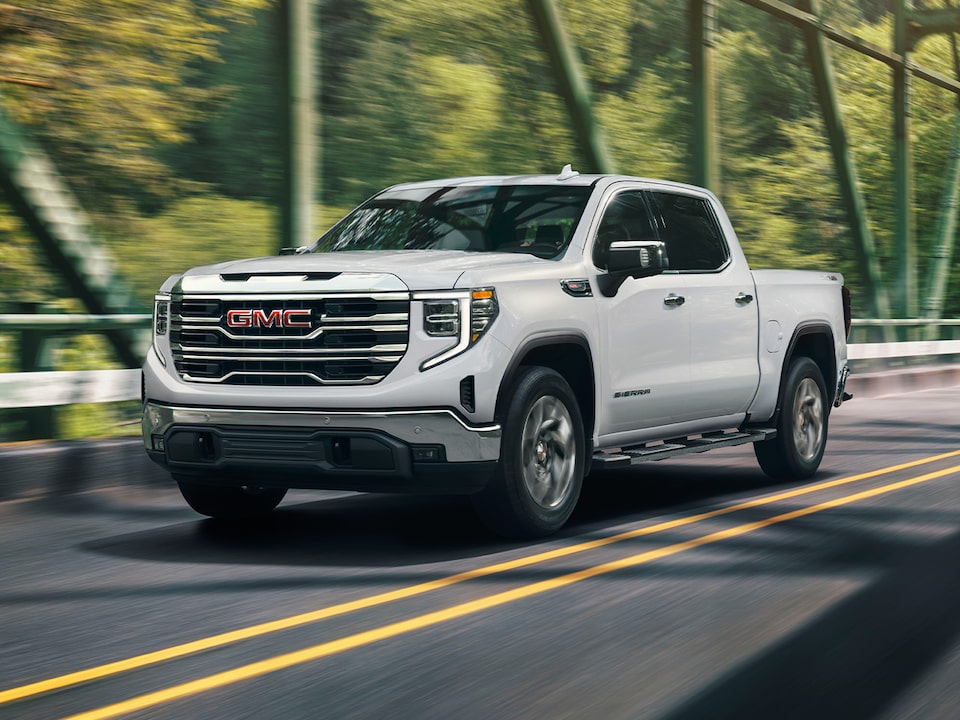 Front Three-Quarters View of a White Sierra Pickup Truck Driving Down the Road