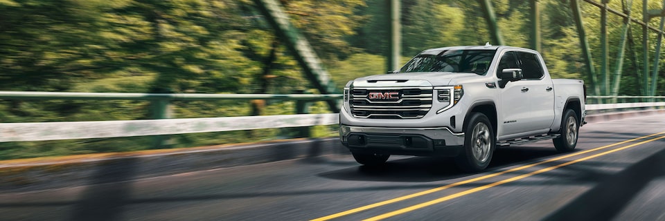 Front Three-Quarters View of a White GMC Sierra Pickup Truck Driving Down the Road