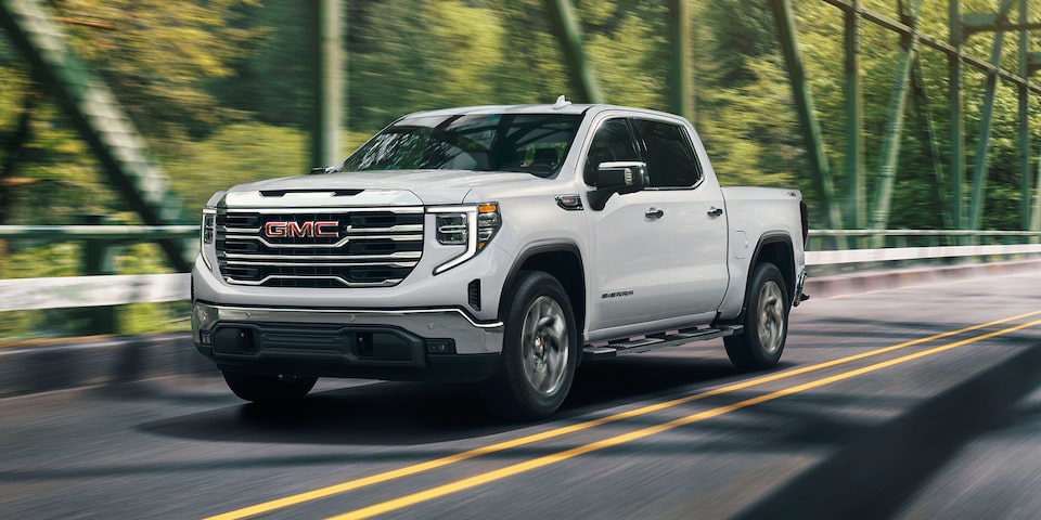 Front Three-Quarters View of a White Sierra Pickup Truck Driving Down the Road