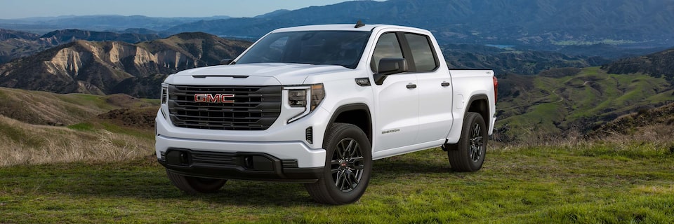 Front Three-Quarter View of a White 2025 GMC Sierra 1500 Pickup Truck Parked in a Valley with Mountains in the Background