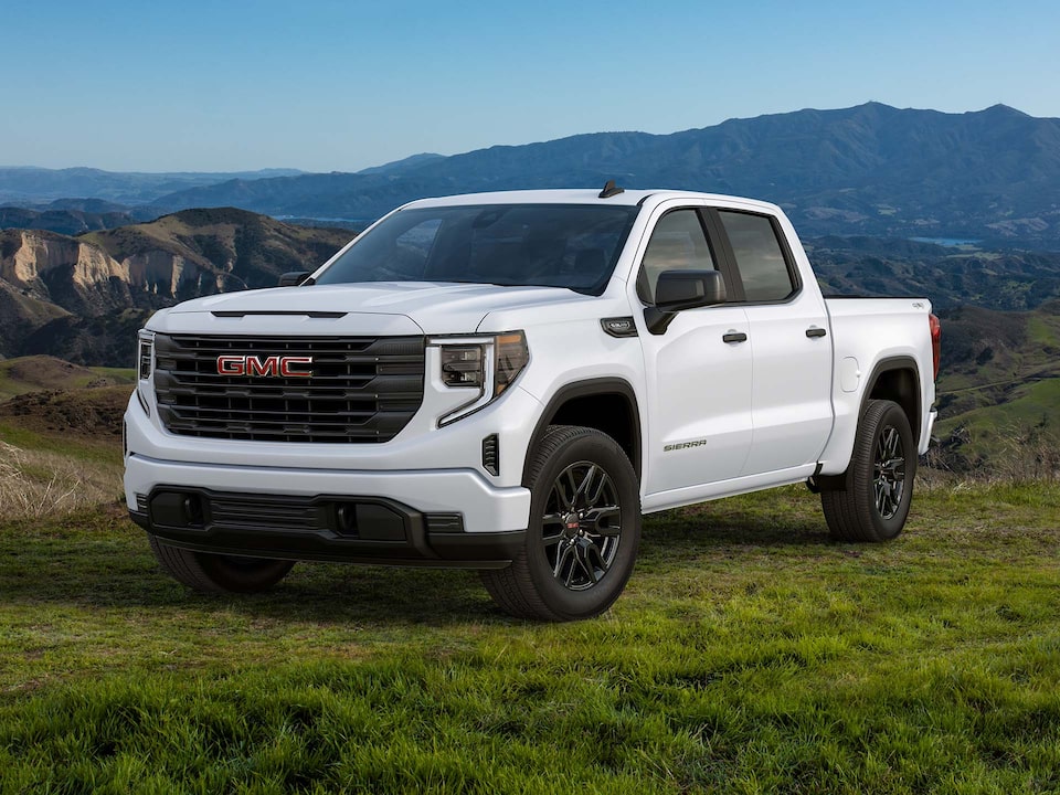 Front Three-Quarter View of a White 2025 GMC Sierra 1500 Pickup Truck Parked in a Valley with Mountains in the Background