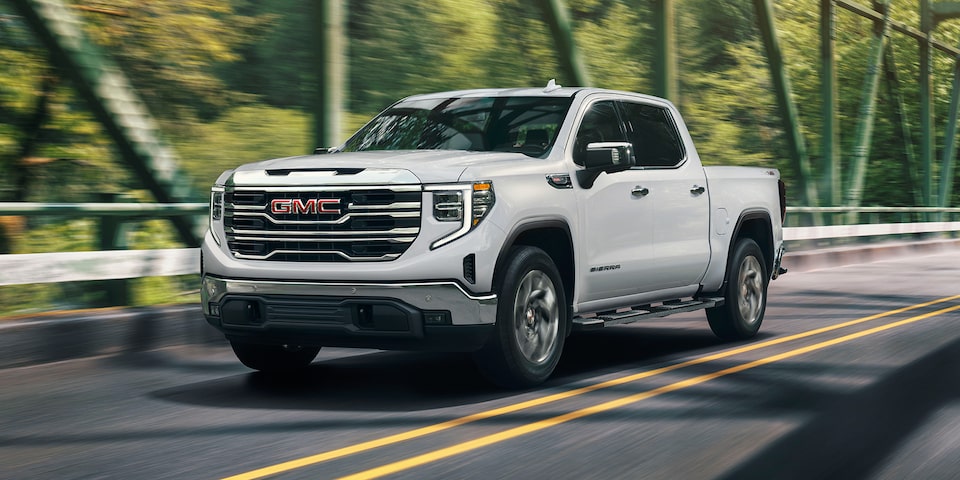 Front Three-Quarters View of a White Sierra Pickup Truck Driving Down the Road