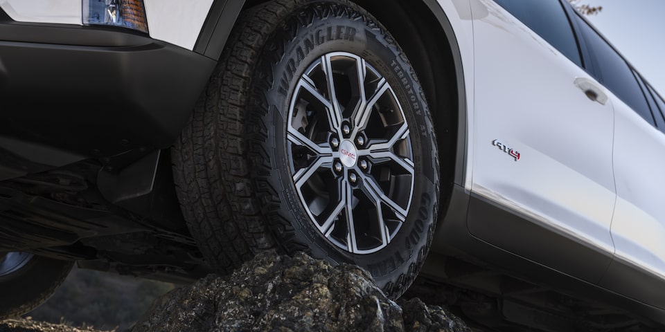 Close up view of the wheel of the 2025 GMC Acadia AT4 atop a rock terrain.