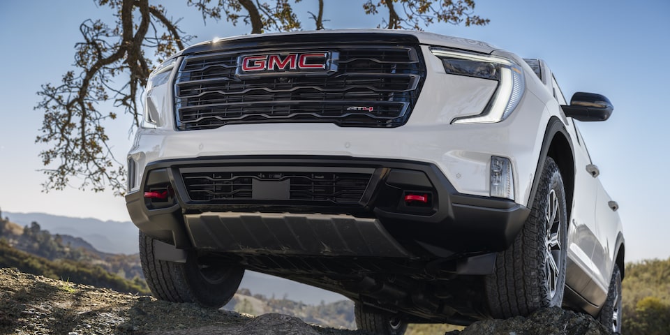 Front view of the 2025 GMC Acadia AT4 driving through a rocky terrain.