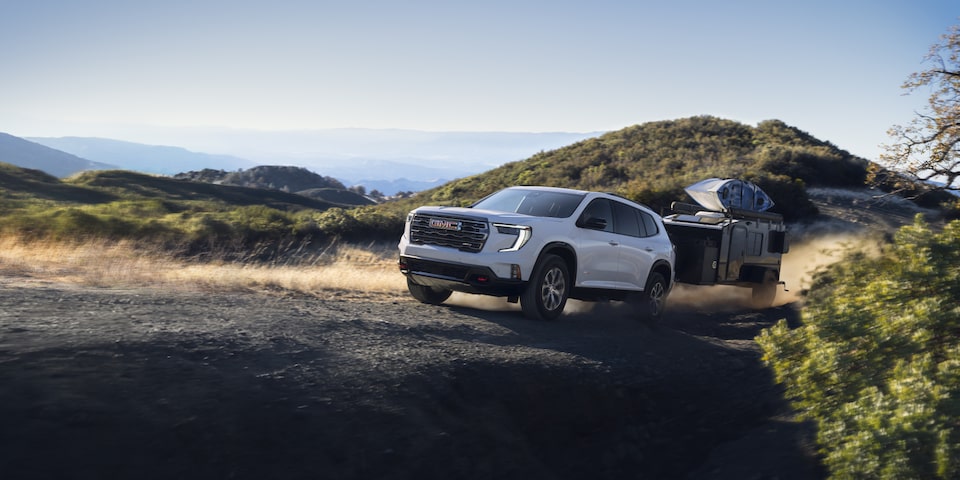 Side view of the 2025 GMC Acadia AT4 towing a trailer on a hillside road.