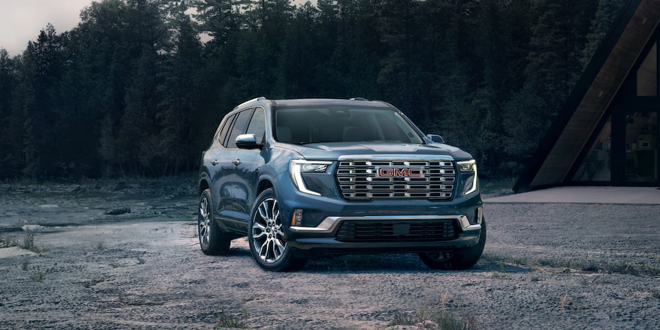 Front view of the 2025 GMC Acadia Denali parked near trees during a gloomy weather.