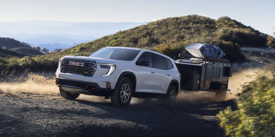 Side view of the 2025 GMC Acadia Denali towing a trailer on a hillside road.