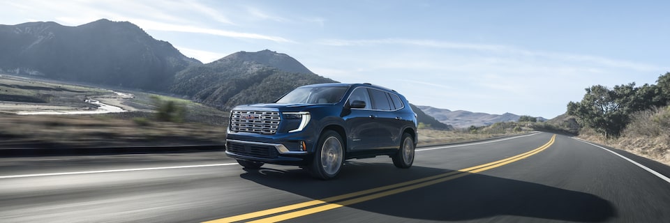 Front-side view of the 2025 GMC Acadia Denali driving fast on the road.