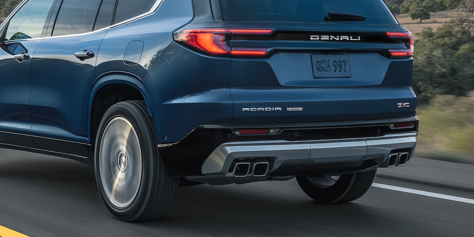 Back-side view of the 2025 GMC Acadia Denali driving alone on a provincial road.