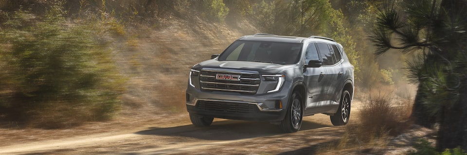 Front-side view of the 2025 Acadia driving fast on a tree-lined road.