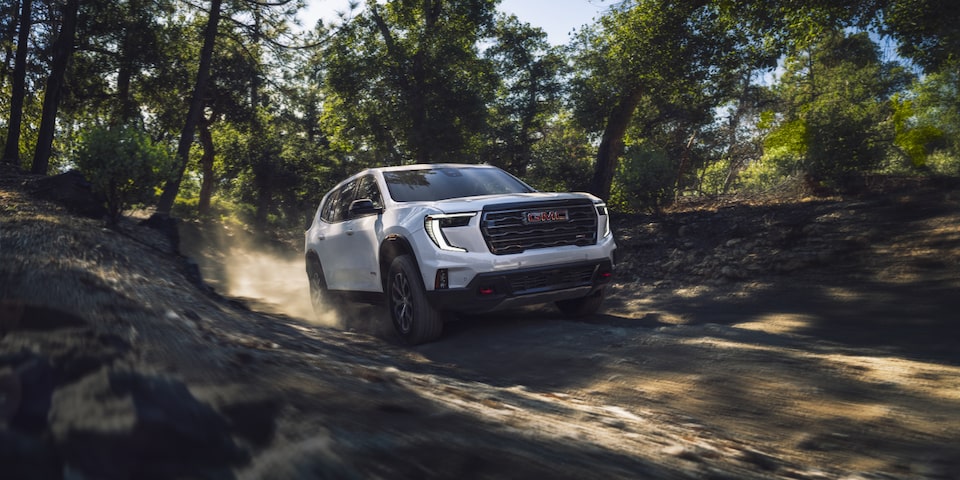 Front-side view of the 2025 GMC Acadia driving fast in the forest.