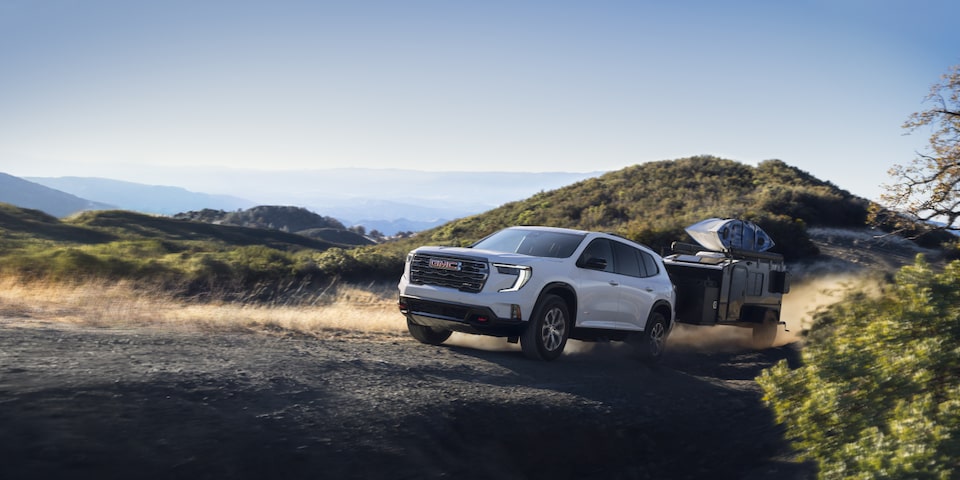 Side view of the 2025 GMC Acadia towing a trailer on a hillside road.