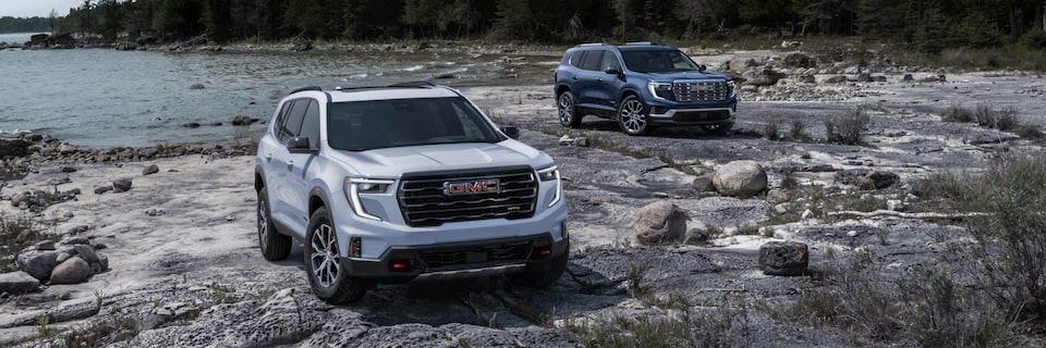 Two 2025 GMC Acadia SUVs parked near a lake.