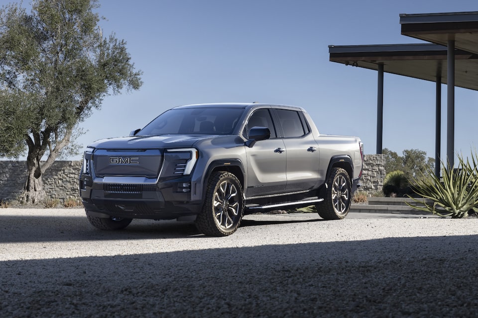 Three-quarters view of a 2025 GMC Sierra EV parked under a clear blue sky.