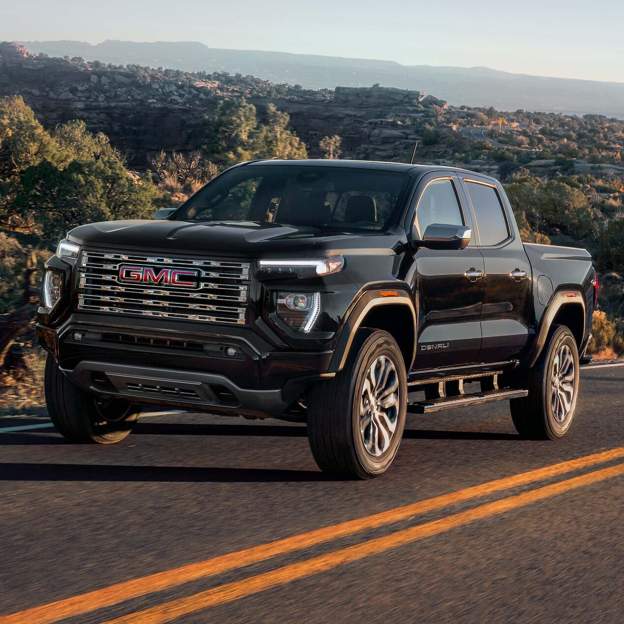 2024 GMC Canyon Denali driving alone a tree-lined road.