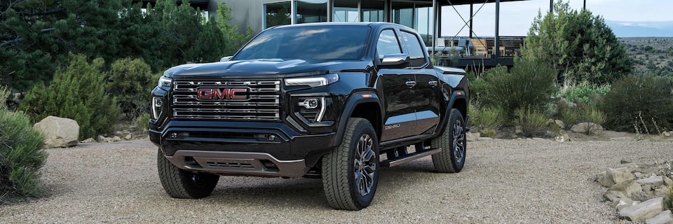 Front-side view of a 2025 GMC Canyon Denali Parked Outside of a Modern Mountain Cabin.