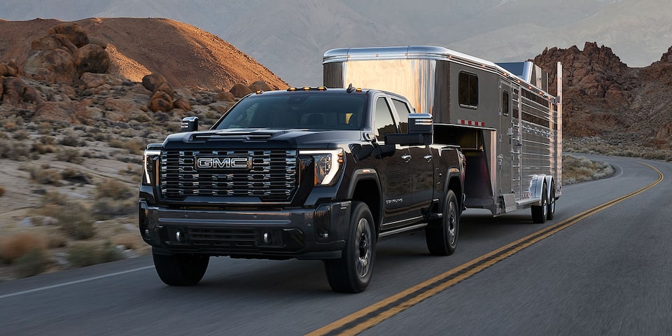 Vue latérale avant du camion GMC Sierra HD Pro/SLE/SLT 2025 qui tire une remorque sur la route.