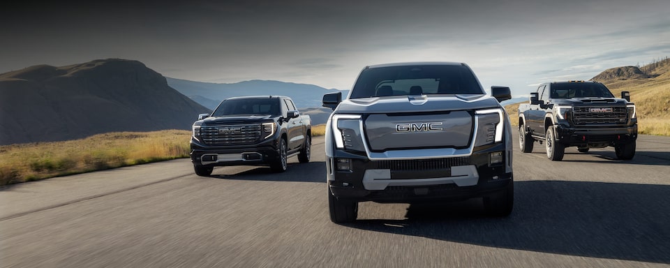 Three GMC Sierra Pickup Trucks Driving Down an Open Road