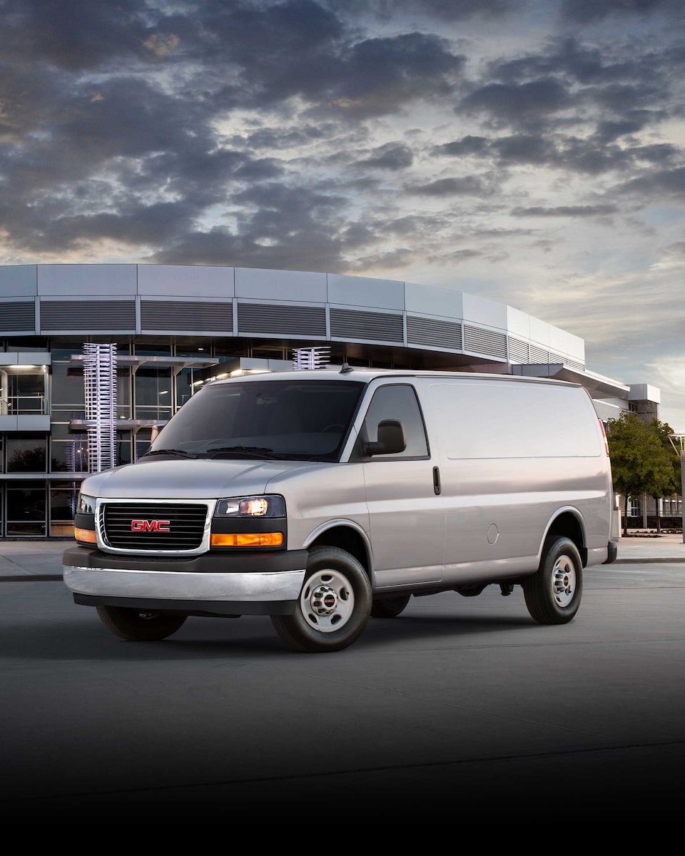 Wide Front Three-Quarters View of a 2024 GMC Savana Cargo Van Parked in Front of a Building