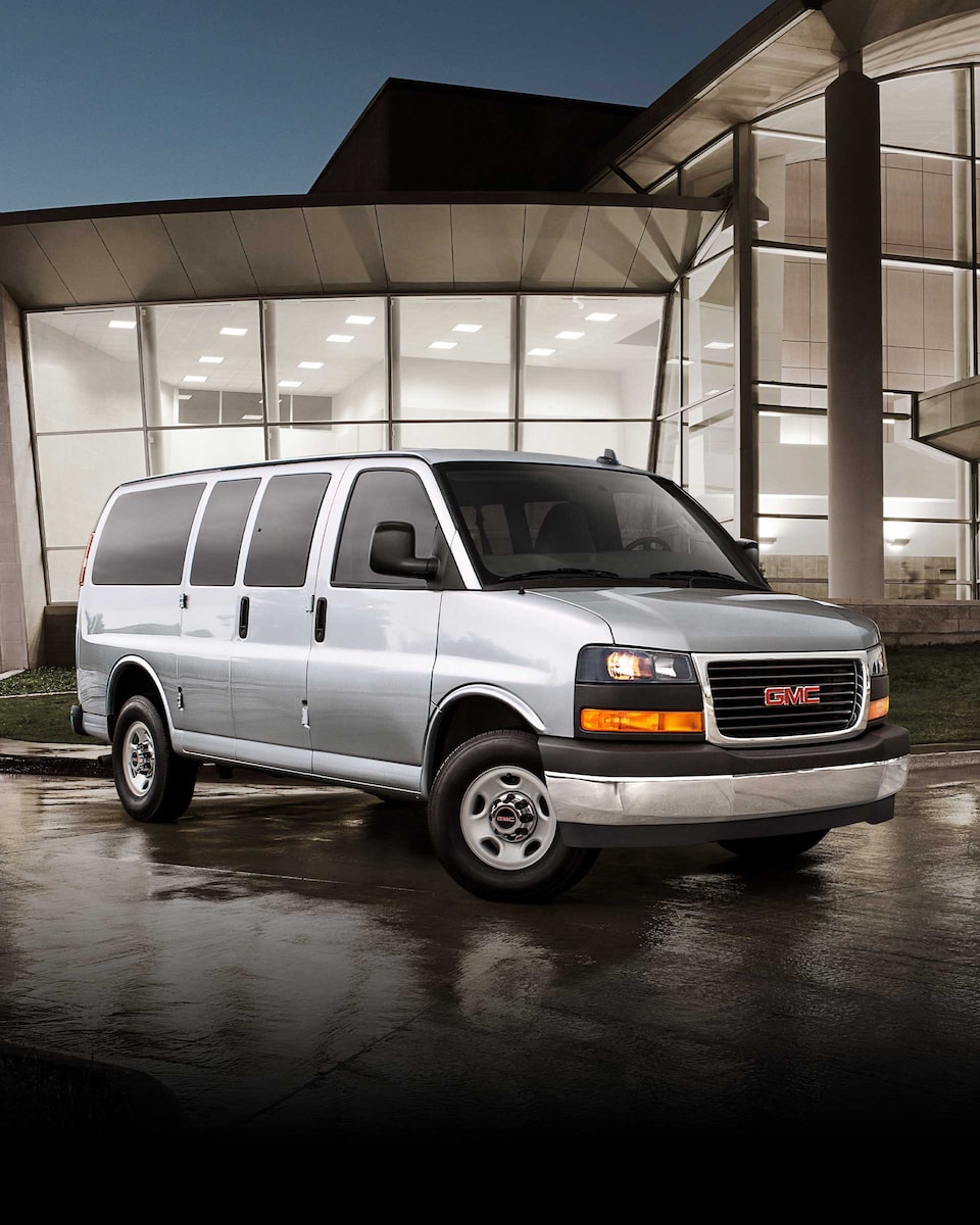 Wide Front Three-Quarters View of a 2024 GMC Savana Passenger Van Parked in Front of a Building