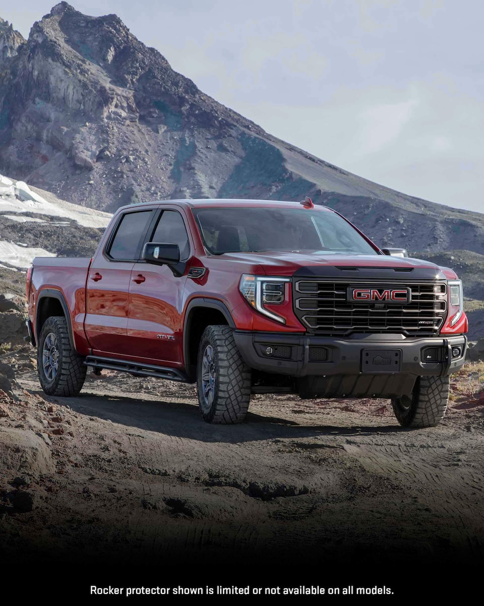 Front Three-Quarters View of a 2024 GMC Sierra 1500 Pickup Truck Parked on a Dirt Path Surrounded by Mountains