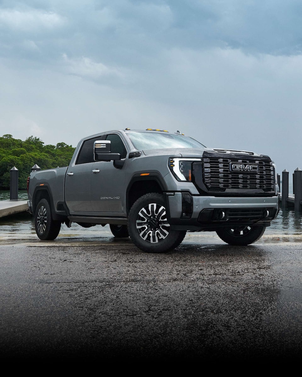 Front Three-Quarters View of a 2024 GMC Sierra HD Pickup Truck Parked on a Paved Road Surrounded by Trees