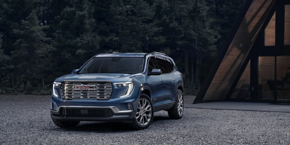 2024 GMC Acadia parked on a pavement near the woods.